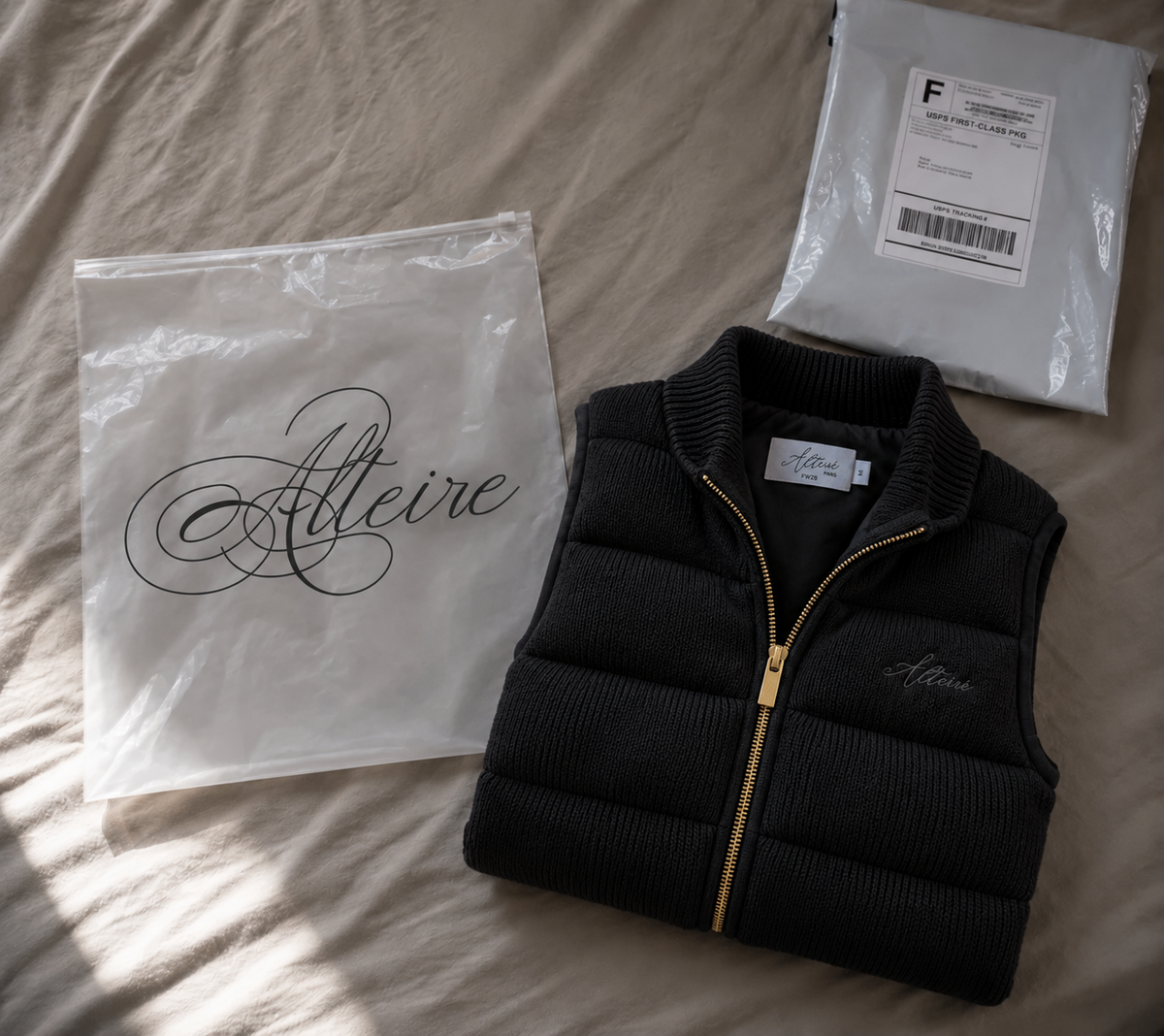 Folded black Alteiré knitted vest beside its branded pouch and protective shipping packaging.